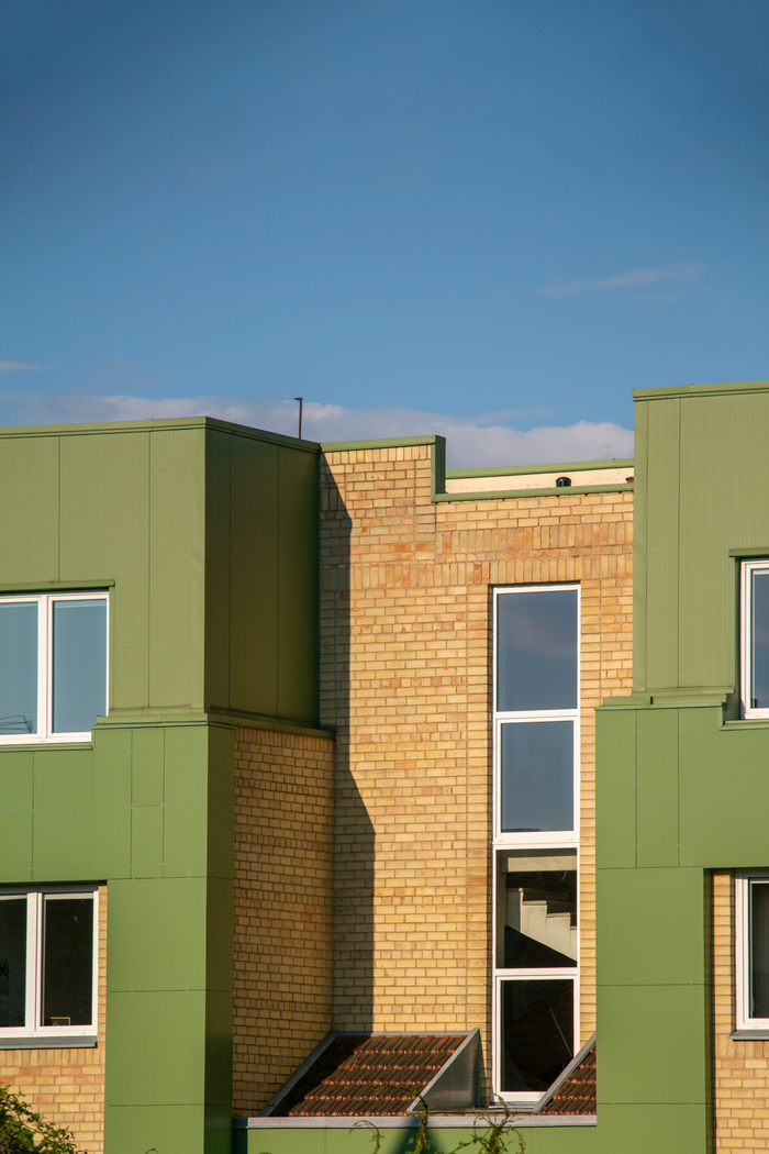 Sunlit modern building exterior with green and brick facade under clear blue sky.