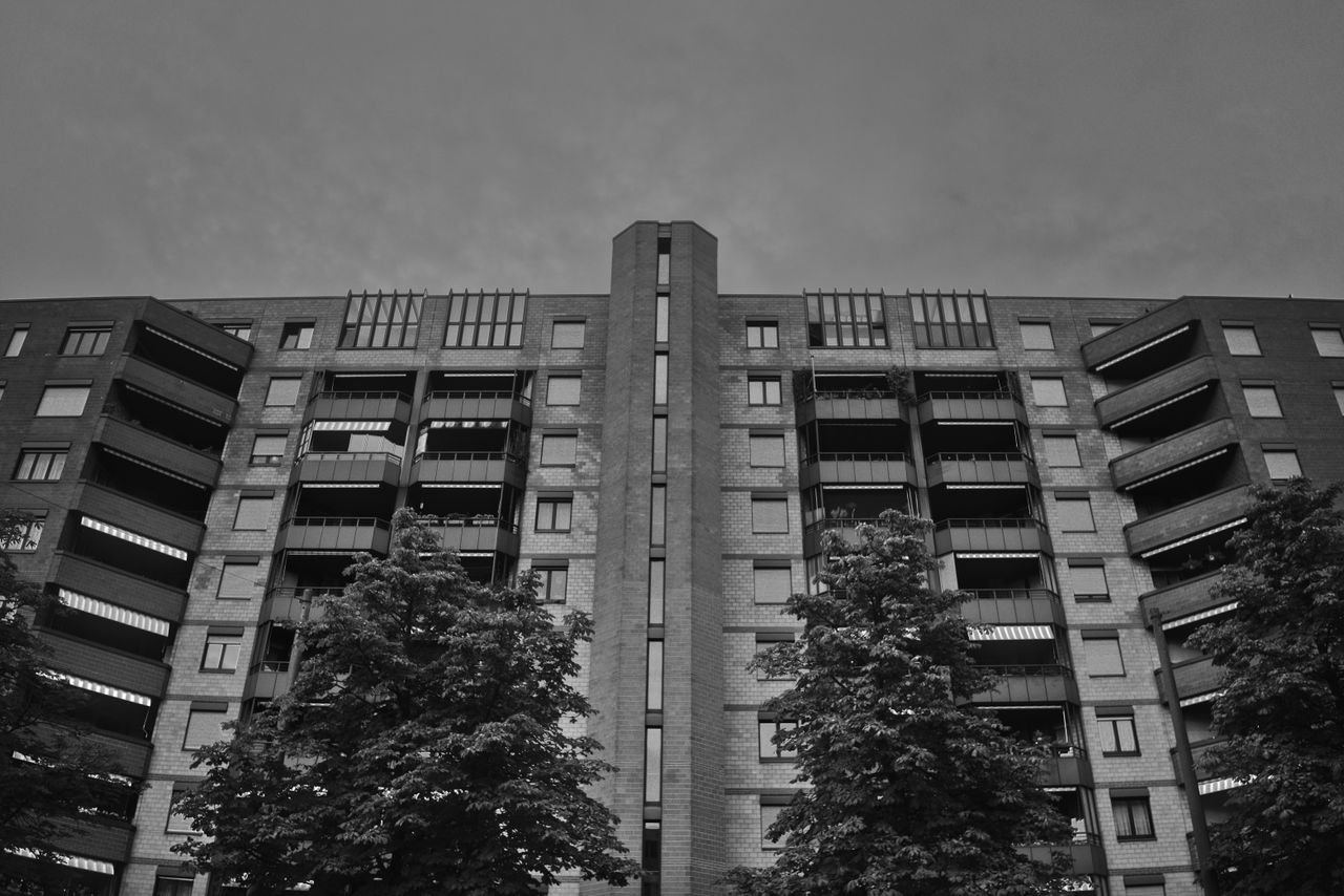 home-services-01 Black and white photo of a modern apartment building facade with trees.